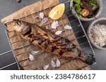 Small photo of Grilled sea bass with lemon on the grid. Grilled spicy fish sea bass . Baked sea Bass fish. Top view