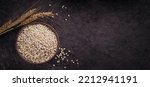 Small photo of Bowl of dry raw broken pearl barley cereal grain on dark background. Cooking pearl barley porridge concept.
