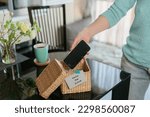 Close up of hand holding smartphone in wicker basket with inscription Device free zone. Woman putting phone into box with different gadgets at home. Digital detox and technology dependance concept