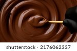Small photo of Hand stirring melted dark chocolate with golden spoon, close up. Liquid hot chocolate. Confectioner prepares chocolate dessert, glaze