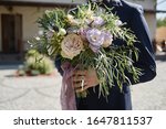 Close up of beautiful bridal bouquet of pink and purple flowers and greenery in groom's hand outdoors, copy space. Wedding concept