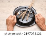 Small photo of On a black plate, an ear, in the hands of a fork and a knife. A symbol of hunger and inept housekeeping is a plate with cutlery and a spikelet against the background of a wooden structure.