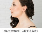 Small photo of Cropped close-up shot of a young woman with asymmetrical silver ear cuffs. Female with metal ear cuffs, side view