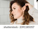 Small photo of Cropped close-up shot of a young woman with two asymmetrical golden ear cuffs. Female with golden ear cuffs, side view.