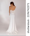 Small photo of Back view of elegant woman in a wedding long dress with open back posing on white background. Fashionable dress with bare shoulders. Wedding details. Slim female model. Jewelry.