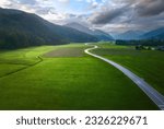 Top drone view of beautiful landscape with alpine mountains, paved highway, hills, fields green grass. Aerial view of beautiful curved rural road in green meadows at dawn in summer in Slovenia
