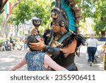 Small photo of Aztec shaman making a ritual to an old woman, using a chalice or calyx; traditional mayan religion dancer using a plume headdress with feathers