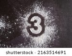 Small photo of The number 3 is written on scattered white flour through a stencil on the dark bacground
