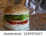 Small photo of vegan burger in tinfoil with tomato and lettuce and fresh cheese-cooked to take away