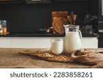Small photo of Milk in a jug and a glass, a wooden spoon with oatmeal and ears of wheat on the table.