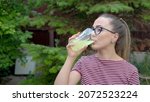 Small photo of A girl with glasses holds a glass with a vitamin drink in her hand and drinks it in one gulp. Maintaining immunity. Healthy lifestyle.