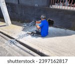 Small photo of Brazil - Sao Paulo - Sao Paulo - November 30, 2023 - Elderly man sitting on sidewalk breaking floor with sledgehammer for plumbing repair