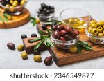 Small photo of A set of green, red and black olives on a light marble background. Various types of olives in bowls and fresh olive leaves. Vegan. Olive fruits. Place for text. Copy space.