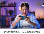 Excited Young Asian woman wearing headset and playing online game on smartphone with live broadcasting on internet.