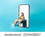 Small photo of Happy Asian woman traveler sitting on the chair and big smartphone with mockup of blank screen, hand holding passport and plane tickets with suitcase isolated on blue background.