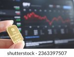 Small photo of A hand holding gold bar with stock forex trade chart blurry background. Investment choice, economy, low vs high risk. Conservative, aggressive investor. Finance money education template presentation.