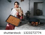 Small photo of Woman holding tray with baklava dessert, indoors. Novruz holiday celebration with beautiful azeri women in traditional Azerbaijani dress and national pastry pakhlava