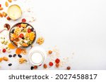 Muesli bowl and ingredients for healthy breakfast. Granola, nuts, dried fruits, flakes, honey and greek yogurt on white table copy space