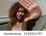 Adult female (34) Latin American afro-descendant curly hair with positive and doubtful attitude, extends the palm of her hand in front of the camera as a stop sign. Lifestyle concept.