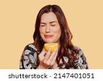 Face portrait of woman wears floral shirt, eating acid lemon doing funny face expression with eyes closed. Studio shot over yellow background. 