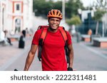 African american delivery man wearing safety helmet smiling and looking at camera in the street.