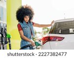 Beautiful woman with afro hair filling her car with gasoline at the gas station.