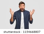 Emotive bearded European male with amazed expression, gestures with hands, keeps palms raised, reacts on sudden news, keeps jaw dropped, poses against white background. Surprisement concept.