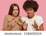 Small photo of Young diverse women feel squeamish, see something unpleasant, express aversion, keep hands over chest, have dissatisfied facial expressions, stand closely to each other against pink background