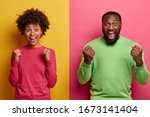 Small photo of Photo of emotional dark skinned female and male clench fists, exclaim and support favorite football team, have overjoyed face expressions, dressed in casual wear, isolated on yellow and pink wall