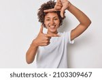 Small photo of Happy woman with curly hair got inspiration imagines hot to capture interesting shot makes frame gesture smiles gladfully dressed in casual t shirt isolated over white background found great spot