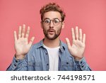 Small photo of I give up! Attractive unshaven stylish man shows palms, demonstrates his innocence, surrenders, isolated over pink background. Handsome young male raises hands, looks puzzled, feels guiltless