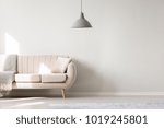 Beige sofa against white, empty wall with copy space in simple living room interior with lamp