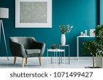 Green armchair against blue wall with silver painting in living room interior with plants