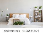 White pillows on wooden bed in minimal bedroom interior with plants and round rug. Real photo