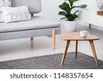 Cup on a wooden coffee table and blurry background with graphic pillows on a gray sofa in a white living room interior