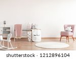 Small photo of Bright scandinavian baby room with rocking horse, white nursery and pink armchairs, posters on the wall