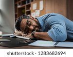 Tired multiethnic businessman sleeping in office. Middle eastern business man with eyeglasses worked late and fell asleep on the computer keyboard. Creative casual man sleeping at his working place