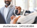 Closeup hand of cardealer giving new car key to customer. Salesman hand giving keys to a client at showroom. Man's hand receiving car keys from african agent in a auto dealership with copy space.