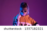 Small photo of Pretty young 20s fashion teen girl model wear glasses blowing bubble gum looking at camera standing at purple studio background, igen teenager in trendy stylish night glow 80s 90s concept, portrait
