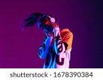 Stylish fashion teenager model wearing hoodie and headphones listening dj music dancing in purple neon lights. Young teen girl enjoy cool music 90s party mix in violet studio background. Copy space.