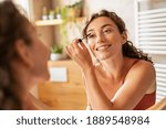 Beautiful woman using mascara on eyelash in bathroom in the morning time. Smiling young woman applying eye make up and looking at mirror. Beauty girl applying black mascara in bathroom at home.