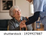 Small photo of Smiling senior woman talking to her general practitioner visiting her at home during virus epidemic. Happy old patient holding hands of caregiver at nursing home and talking. Reassurance and console.