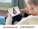 Back view of senior woman sitting in wheelchair making video call with her doctor while staying at home during covid pandemic. Sick woman in online consultation from home: distance and tele health.