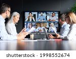 Global corporation online videoconference in meeting room with diverse people sitting in modern office and multicultural multiethnic colleagues on big screen monitor. Business technologies concept.