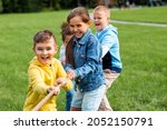 Small photo of childhood, leisure and people concept - group of happy kids playing tug-of-war game and running at park