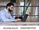 Small photo of Side view of serious adult concentrated focused Indian Hispanic boss ceo businessman using typing on computer pc laptop working in contemporary office, accounting analysing report financial data.