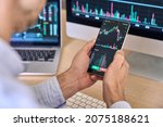 Small photo of Crypto trader investor broker using smartphone app analyzing financial data stock market price on cell phone, checking online trading platform application, buying cryptocurrency, over shoulder view.