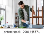 Small photo of furniture renovation, diy and home improvement concept - man in gloves with paint brush painting old wooden table in grey color