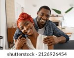 Portrait of mid adult happy african american couple hugging at home while sitting on couch. Portrait of mature man with his woman wearing traditional turban looking at camera. Black mid adult couple. 