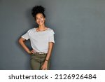 Portrait of young african american woman standing with hands on waist and looking at camera. Confident stylish black girl standing against grey background. Happy afro girl smiling with copy space.